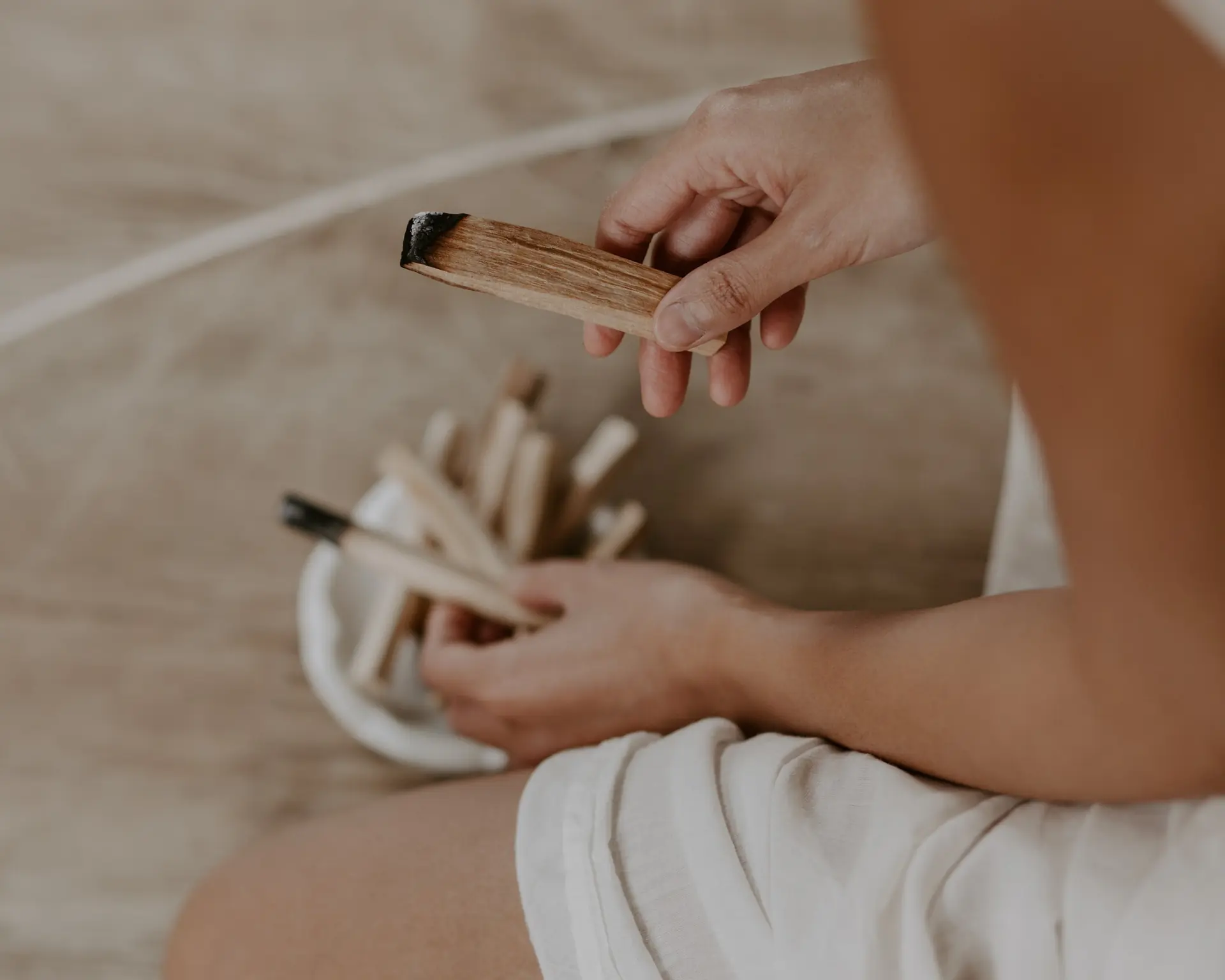 Hands holding a bundle of palo santo sticks over a ceramic bowl