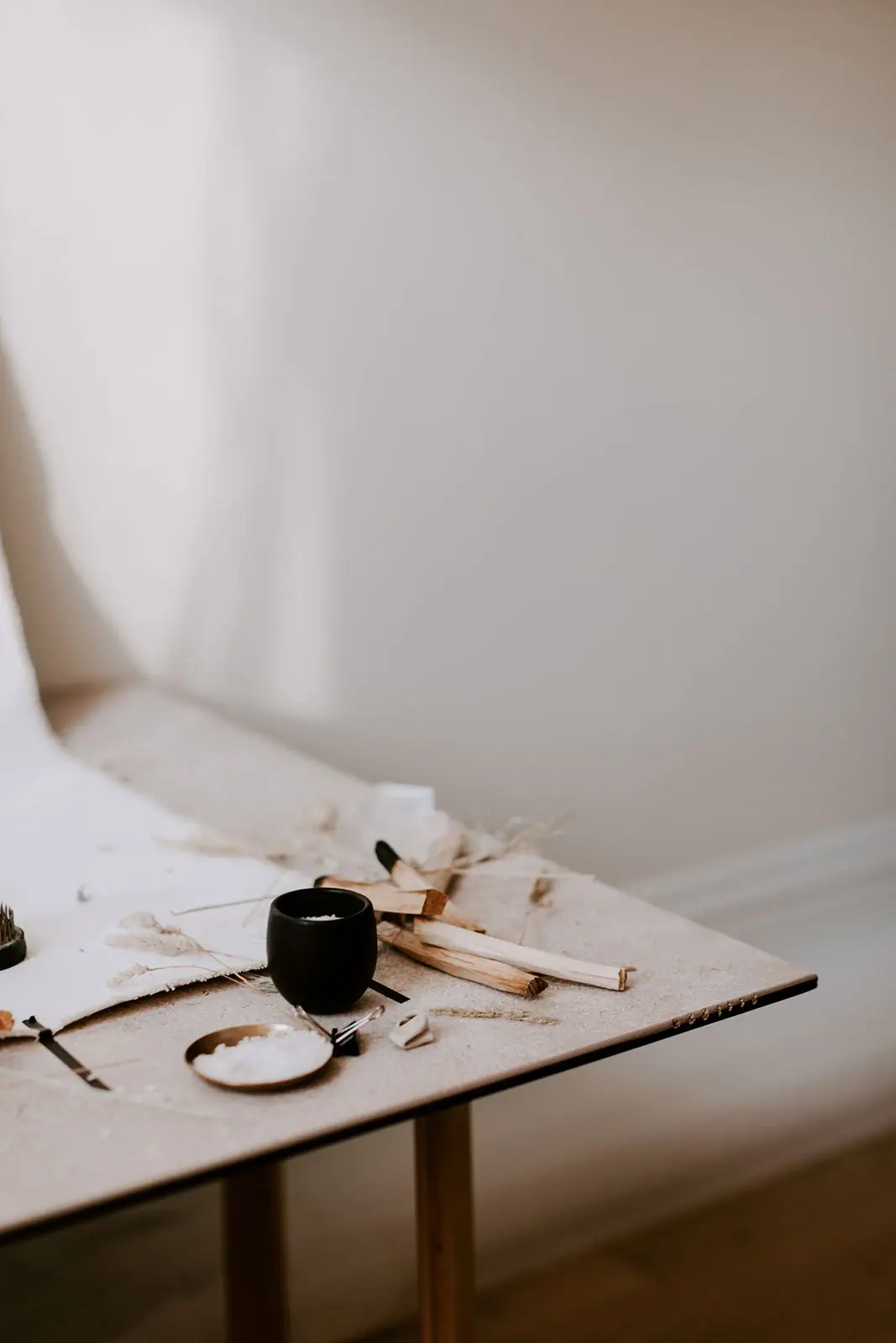 Palo santo sticks, dried botanicals and a small brass dish of salt laid out on a pale table in a sunlit room