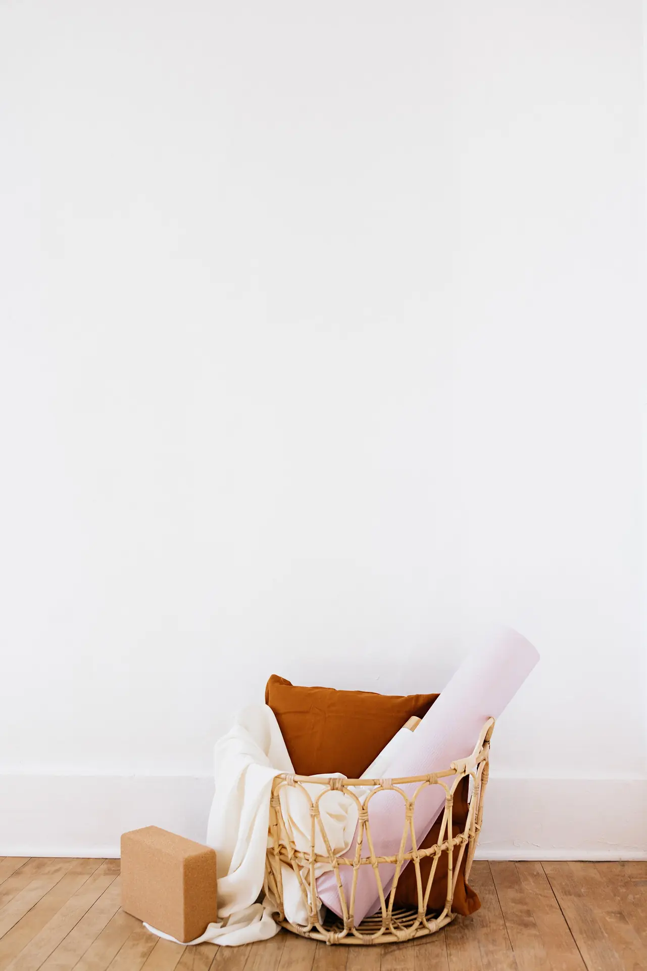 A woven basket holding folded blankets, a bolster and a yoga block