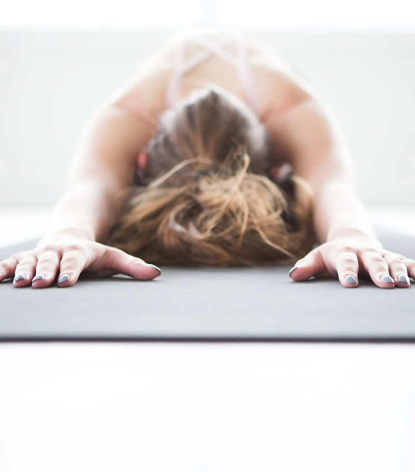A student resting in a forward fold with her hands spread wide on the mat