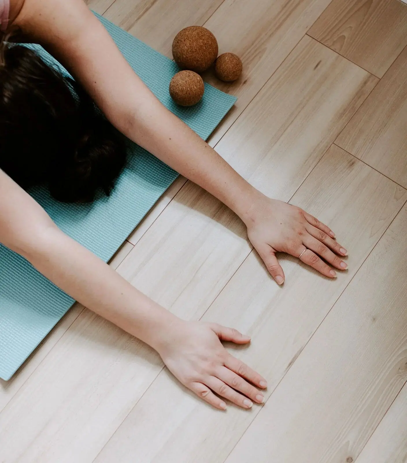Hands reaching forward on a yoga mat on a pale wood floor