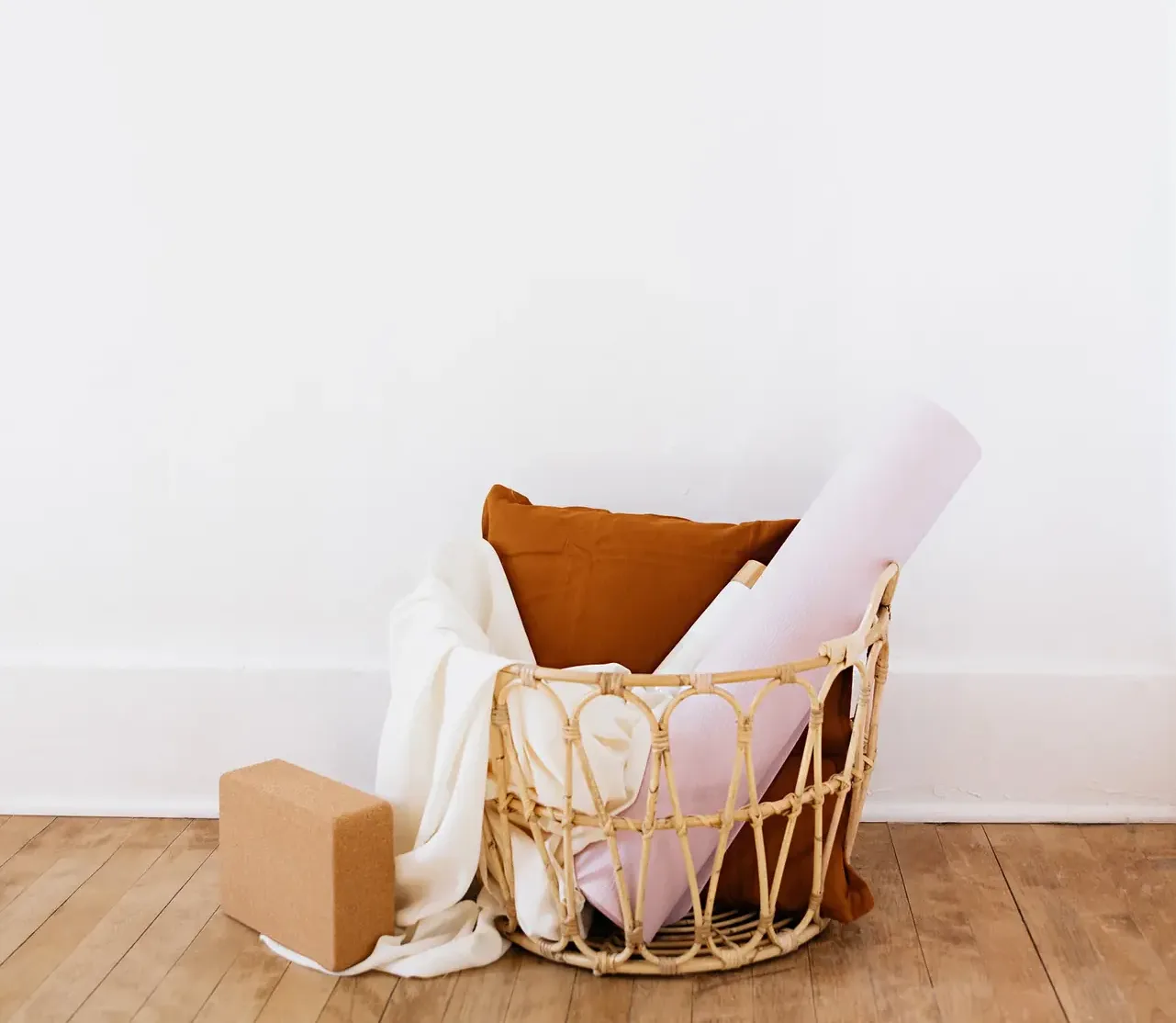 A woven basket holding folded blankets, a bolster and a yoga block